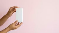 A person with medium skin tone holds a blank white rectangular card or product packaging against a soft pink background, suitable for branding, mockups, and marketing materials.