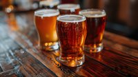 Craft beer flight tasting glasses filled with amber ale on rustic wooden table in brewery taproom for sampling different brews and flavors.