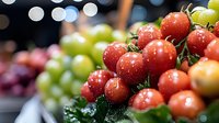 Fresh red grapes with water droplets at farmers market display with colorful fruit selection in background for healthy eating and organic produce concepts.