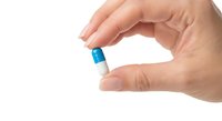 Hand holding blue and white capsule pill between fingers on white background isolated for medical healthcare pharmaceutical design.