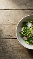 Fresh radish and microgreens salad in speckled white bowl on rustic wooden table, overhead view with copy space for healthy eating and recipe content.