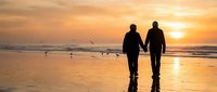 Two people walking together on beach at sunset with golden sky and ocean waves reflecting warm light creating romantic peaceful atmosphere.