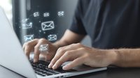 Male hands typing on laptop keyboard with glowing email icons floating above, representing digital communication and message sending in business environment.