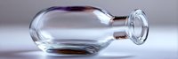 Empty transparent glass bottle lying on side with soft shadows and reflections on light surface, minimalist composition showing clarity and purity of glassware.