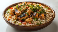 Grilled chicken pieces glazed with teriyaki sauce served on brown rice with fresh herbs and vegetables in wooden bowl, appetizing Asian fusion cuisine.