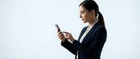 Young professional woman with dark hair and South Asian ethnicity wearing navy business blazer, holding and looking at smartphone against white background for corporate communications.