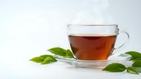 Clear glass teacup filled with amber herbal tea surrounded by fresh green leaves on white background for wellness and relaxation concepts.
