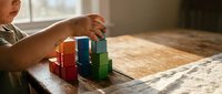 Child playing with colorful wooden building blocks on table, developing fine motor skills and creativity through educational toy construction play.