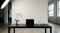Modern minimalist home office workspace with black desk, laptop computer, white orchid plant and wine glass in contemporary loft interior with natural light.