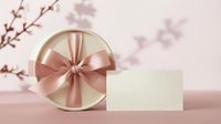 Elegant round gift box with pink satin ribbon bow and blank card on soft pink background with cherry blossom branches for special occasions and celebrations.