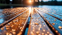 Raindrops on wooden deck planks at sunset create magical light reflections and bokeh effect, water droplets glistening on natural wood surface in golden hour light.