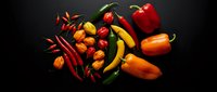 Colorful assortment of fresh hot peppers and chili varieties arranged on dark background for culinary cooking and spicy food preparation.