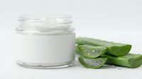 Natural aloe vera moisturizing cream in glass jar with fresh cut aloe leaves showing gel texture for skincare and beauty treatments.