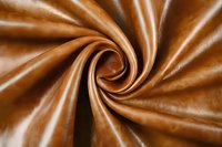 Luxurious brown satin fabric swirled in elegant spiral pattern creating dynamic folds and curves with smooth glossy texture and rich caramel tones.