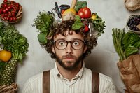 Young bearded man in glasses and curly hair surrounded by fresh vegetables and produce. Creative food portrait with organic ingredients and healthy eating concept.