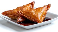 Golden crispy samosas with flaky pastry served on white plate with dark dipping sauce, traditional Indian appetizer snack food for restaurant menu design.