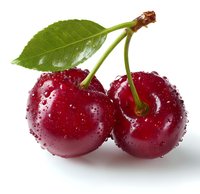 Fresh ripe cherries with water drops and green leaf isolated on white background. Macro shot of wet red sweet fruit for packaging design and food industry.