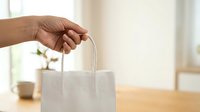 Close-up of hand holding white fabric shopping bag with handles on wooden table, suitable for retail, commerce, and sustainable packaging concepts.