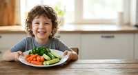 Happy young boy with curly hair enjoying healthy vegetables at kitchen table, promoting nutritious eating habits and childhood wellness at home.