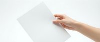 Hand holding blank white paper sheet against light background for mockup design templates and presentations.