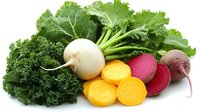 Fresh organic vegetables including kale, turnip, golden beets and red beets arranged on white background, showing whole and sliced produce for healthy eating concept.