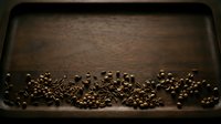 Roasted coffee beans scattered on dark metal baking tray, overhead view. For coffee shop marketing, cafe menus, beverage packaging, and culinary content.