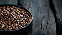 Fresh roasted coffee beans in black ceramic bowl on rustic wooden table background with dramatic lighting and copy space for menu design.