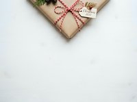 Wrapped gift box with kraft paper, red and white twine bow, evergreen sprigs and gift tag on white background for holiday greeting cards and seasonal marketing materials.