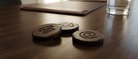 Wooden keychains with engraved symbols arranged on dark desk surface next to tablet and water glass, suitable for product photography and promotional materials.