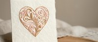 Elegant ornate heart with intricate swirls and flourishes embossed on textured white paper for romantic greeting cards and wedding stationery designs.