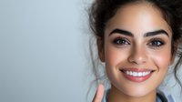 Young Hispanic woman with natural makeup and radiant smile against light background, showing healthy white teeth and glowing skin. Professional portrait for dental and beauty.