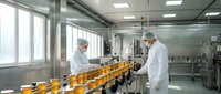 Two pharmaceutical technicians in white protective suits monitoring orange bottle production line in sterile manufacturing facility with quality control equipment.