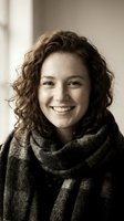 Young woman with curly brown hair smiling warmly while wearing cozy knit scarf in soft natural lighting for lifestyle and fashion content.