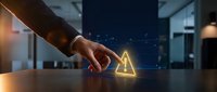 Professional businessman touching glowing warning triangle symbol on modern office desk representing cybersecurity alerts and digital risk management.