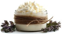 Homemade body butter cream in glass jar decorated with twine rope, topped with whipped texture and fresh lavender flowers on white background.