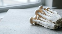 Cluster of dried mushrooms with tan caps and white stems arranged on neutral surface, suitable for culinary, wellness, and botanical content.