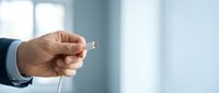 Hand of a man wearing a business suit holding an unplugged electrical cord with connector against a blurred office background, representing disconnection or power issues.