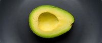 Halved avocado with pit removed on dark surface, showing fresh green flesh and creamy texture for culinary and food styling projects.