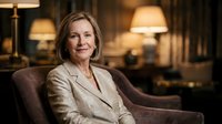 Professional mature Caucasian businesswoman in beige blazer sitting confidently in luxury hotel lobby with warm lighting for corporate presentations.
