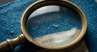 Magnifying glass with investigation text on blue textured surface for detective work, research analysis, forensic examination and crime solving concepts.