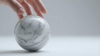 Hand protecting marble sphere on white surface symbolizing care, protection and precious value in minimalist setting.