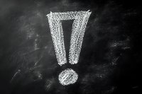 White chalk exclamation mark drawn on dark blackboard background with textured dusty surface, showing emphasis and attention symbol.