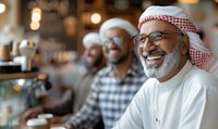 Middle Eastern senior man in traditional white thobe and red keffiyeh wearing glasses, laughing joyfully at coffee shop with friends in background, expressing happiness.