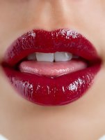 Sensual close-up of glossy red lips with white teeth showing, featuring rich burgundy lipstick with wet shine effect, suitable for beauty and cosmetic advertising.
