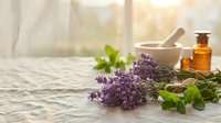 Fresh lavender sprigs with mint leaves on wooden table beside mortar pestle and amber bottles for natural aromatherapy and herbal medicine preparation.
