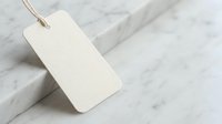 Blank beige paper tag with string on white marble surface for product labeling, pricing, gift wrapping and branding mockup designs.