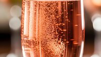 Rose champagne with bubbles in elegant flute glass against blurred bokeh background for celebration and luxury dining occasions.