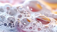 Macro photography of soap bubbles with pink and orange gradient background creating abstract pattern of spherical formations with light reflections and transparency.