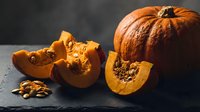 Fresh orange pumpkin sliced open showing seeds and flesh on dark slate surface with walnuts for autumn cooking and seasonal recipes.