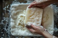 Hands washing white cotton fabric in soapy water with foam and bubbles, showing traditional laundry process and sustainable cleaning methods at home.